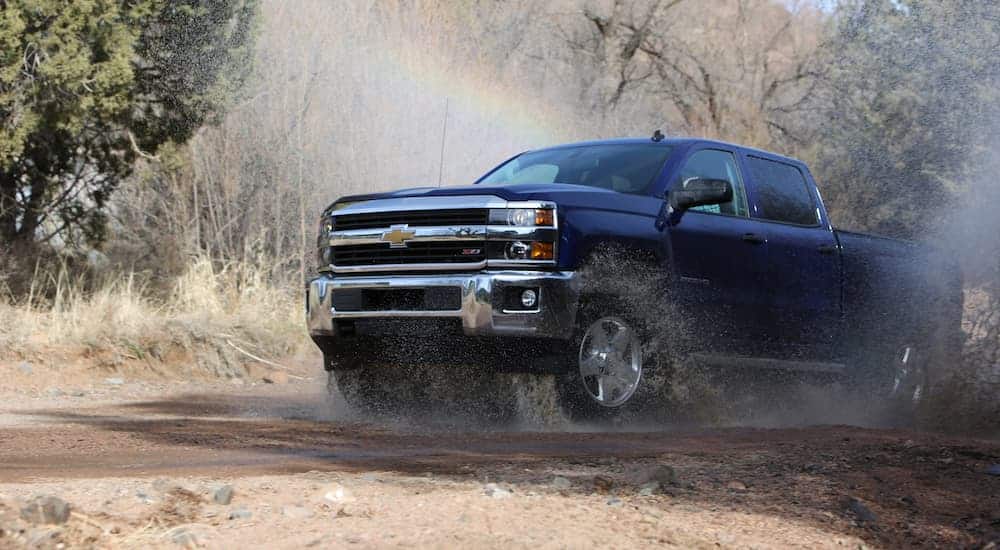 A blue 2016 Chevrolet Silverado is driving though a puddle kicking up water with a refracted rainbow.