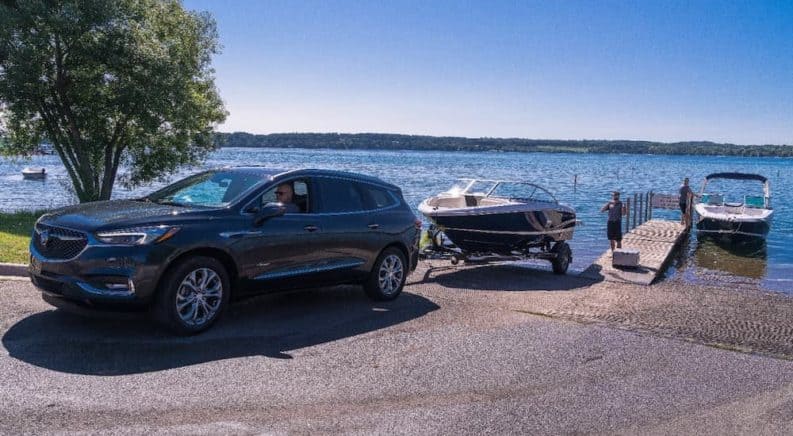 A blue 2019 used Buick Enclave Avenir is backing a boat in to the water near a dock.