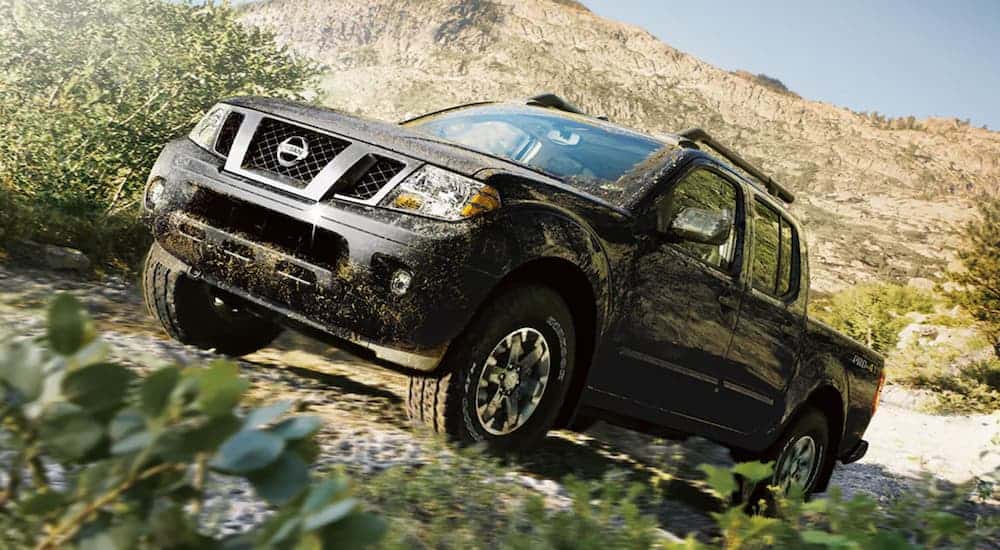 A muddy black 2020 Nissan Frontier is off-roading up a trail.