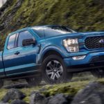 A blue 2021 Ford F-150 STX is driving up a mountain road.