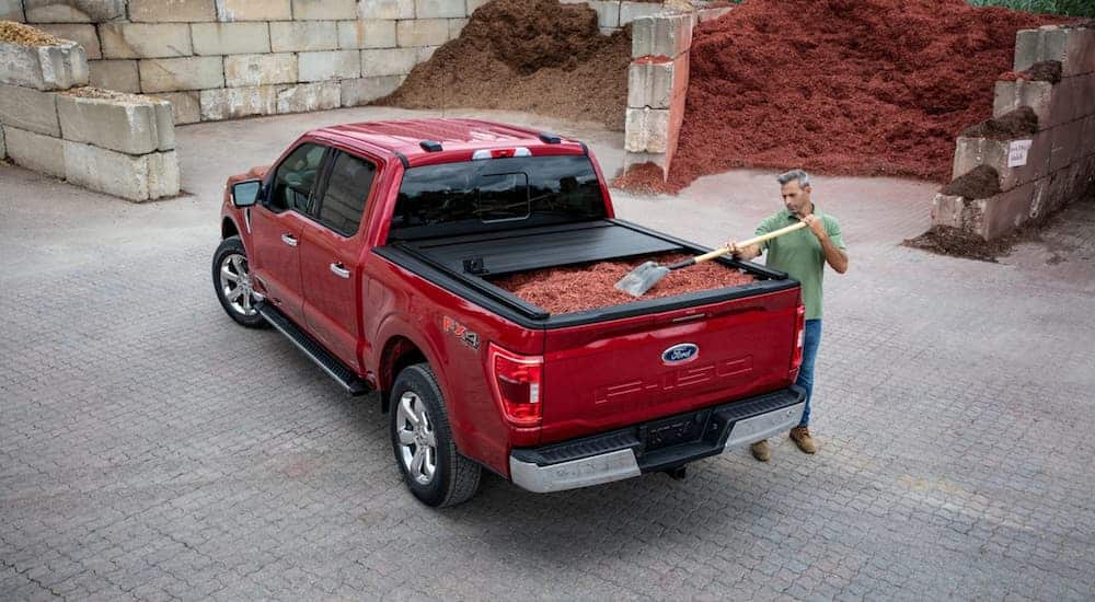 A red 2021 Ford F-150 is having its bed filled with mulch.