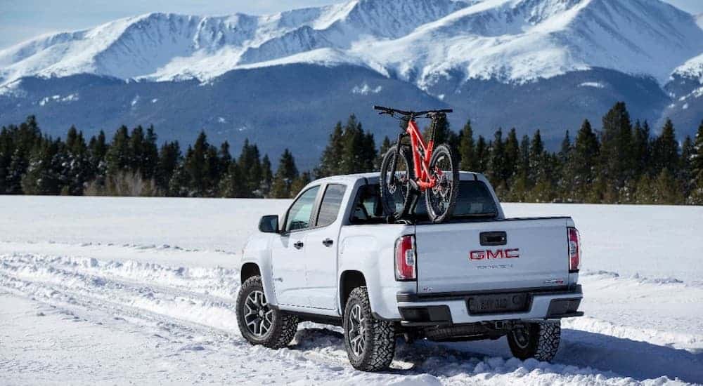 A white 2021 GMC Canyon AT4 is parked in the snow with a red bike mounted on the truck bed.