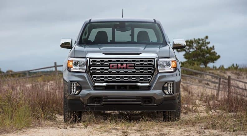 A silver 2021 GMC Canyon Denali is parked in the grass with a fence in the background after leaving a GMC dealer.