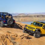 Two 2021 Jeep Wranglers, a blue, and a yellow, are parked on rocks in the desert after leaving a Jeep dealer.