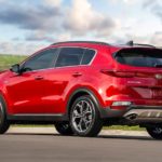 A red 2021 Kia Sportage is parked on the asphalt with grass and sky in the background.