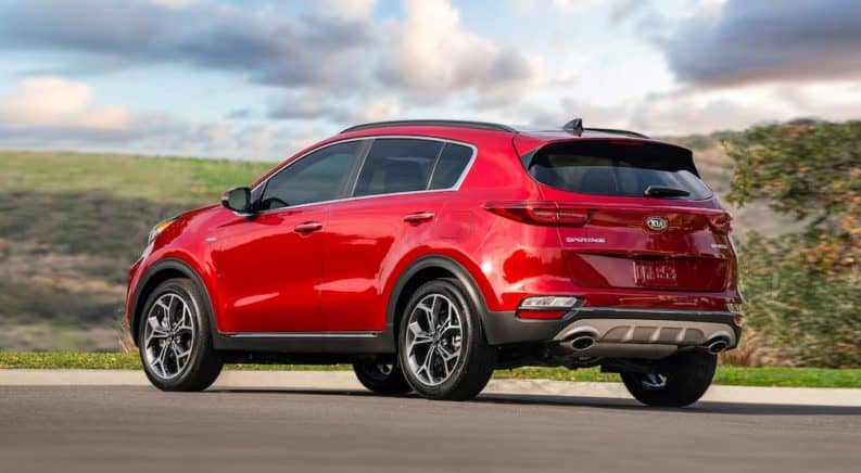 A red 2021 Kia Sportage is parked on the asphalt with grass and sky in the background.