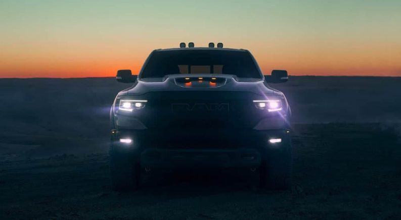 A grey 2021 Ram 1500 TRX is parked in the desert at dusk with its headlights illuminated.