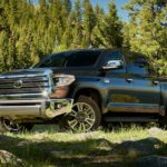 A black 2021 Toyota Tundra is parked on grass in front of pine trees.