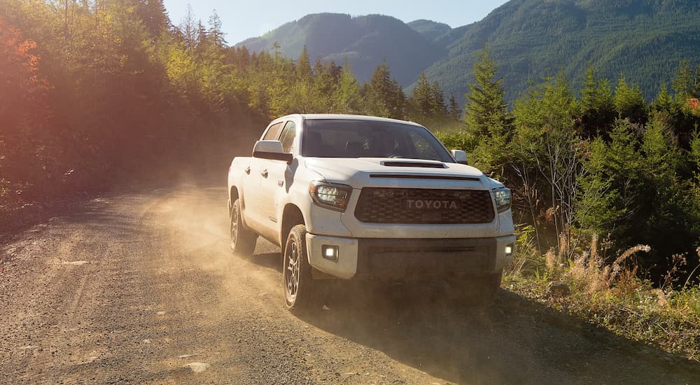 A white 2021 Toyota Tundra TRD is driving on a dirt road in front of mountains.