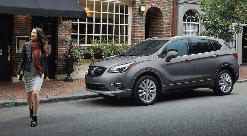 A woman is walking away from a grey 2020 Buick Envision in front of a brick building.