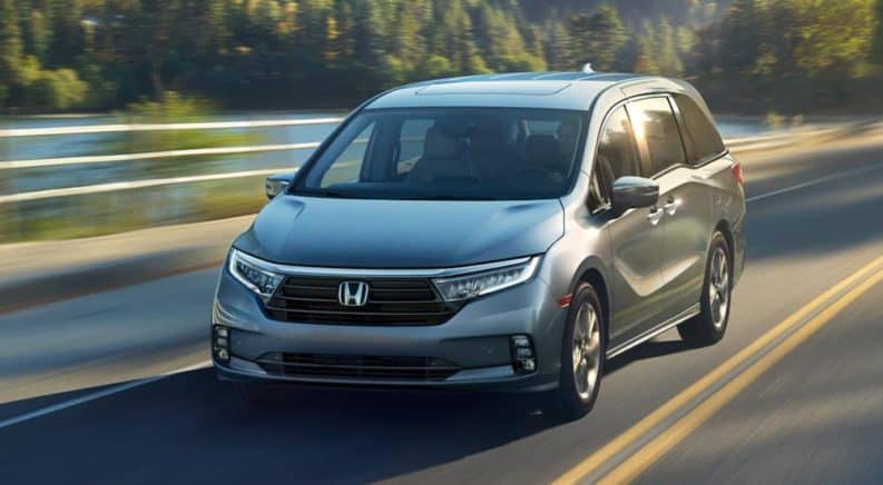 A grey 2021 Honda Odyssey is driving past a white fence after leaving a Honda dealer near me.