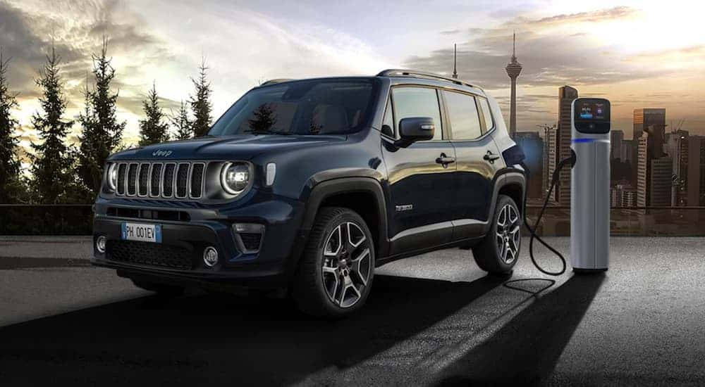 A black 2021 Jeep Renegade 4xe, one of the UK Jeep SUVs, is plugged in to charge in front of a city.