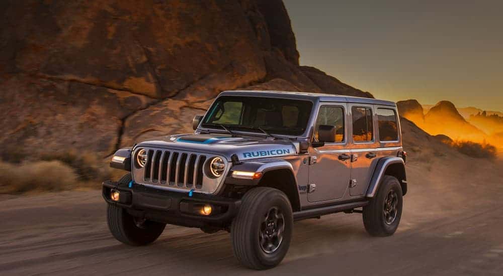A silver 2021 Jeep Wrangler 4xe is driving on a desert road at dusk.