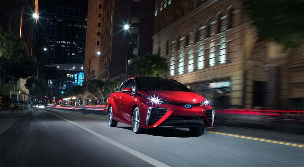 A red 2020 Toyota Mirai is driving through a city at night after leaving the Toyota dealership.