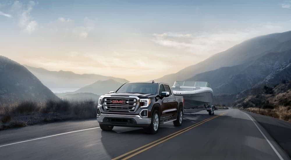 A black 2019 Used GMC Sierra is towing a boat through a mountain range.