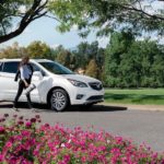 A white 2021 Buick Envision is shown from the side next to a woman holding a yoga mat after winning the 2021 Buick Envision vs 2021 Acura RDX comparison.
