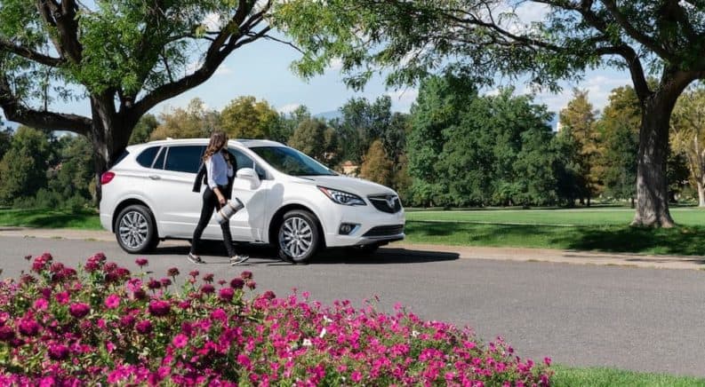 A white 2021 Buick Envision is shown from the side next to a woman holding a yoga mat after winning the 2021 Buick Envision vs 2021 Acura RDX comparison.