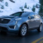 A blue 2021 Cadillac XT5 is driving down the road past snow and trees.