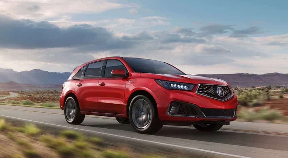 A red 2020 Acura MDX is driving down the highway with mountains in the background.