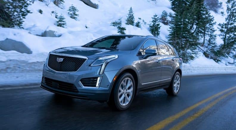 A blue 2021 Cadillac XT5 is driving down a road past snow and trees after winning the 2021 Cadillac XT5 vs 2020 comparison.