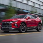 A red 2021 Chevy Blazer RS is driving through the city past a blurred building.