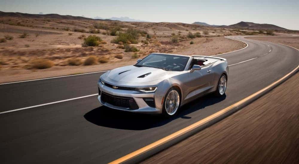 A silver 2021 Chevy Camaro SS convertible is driving on a desert highway.