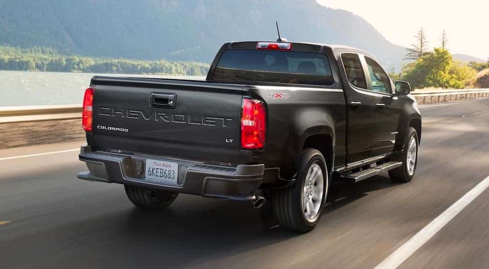 A black 2021 Chevy Colorado is driving down the road past a lake.