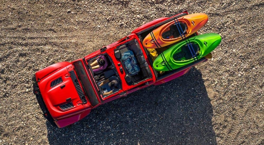 A red 2021 Jeep Gladiator is shown from a high angle parked in the dirt with a orange and a green kayak in the bed.