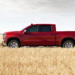 A red 2021 Chevy Silverado 1500 Trailboss LT is parked in a field next to a man after winning the 2021 Chevy Silverado 1500 vs 2021 Ford F-150 comparison.