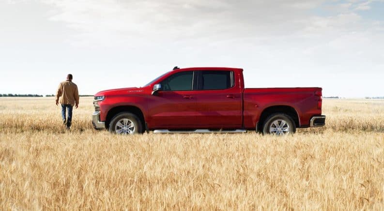 A red 2021 Chevy Silverado 1500 Trailboss LT is parked in a field next to a man after winning the 2021 Chevy Silverado 1500 vs 2021 Ford F-150 comparison.