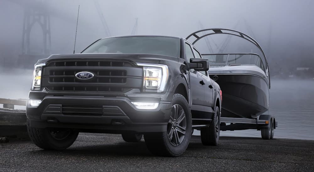A black 2021 Ford F-150 is towing a boat in the mist with its lights illuminated.