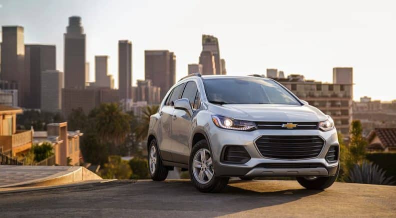A silver 2021 Chevy Trax is parked with a city skyline in the background.