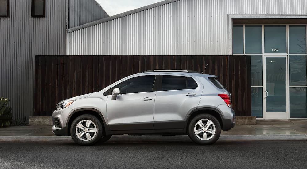 A silver 2021 Chevy Trax is parked outside a warehouse shown in profile.
