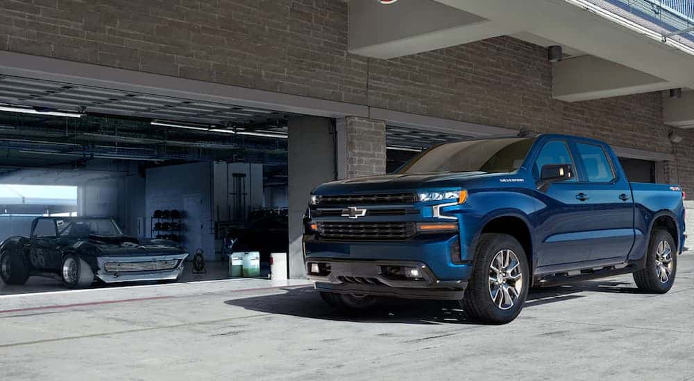 A blue 2021 Chevy Silverado 1500 RST is parked in front of a garage with a race car.