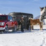 A red 2021 Ford F-150 King Ranch is parked in the snow with a couple, two horses, and a trailer.