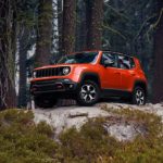 A red 2021 Jeep Renegade Trailhawk is parked on a large rock in the woods.