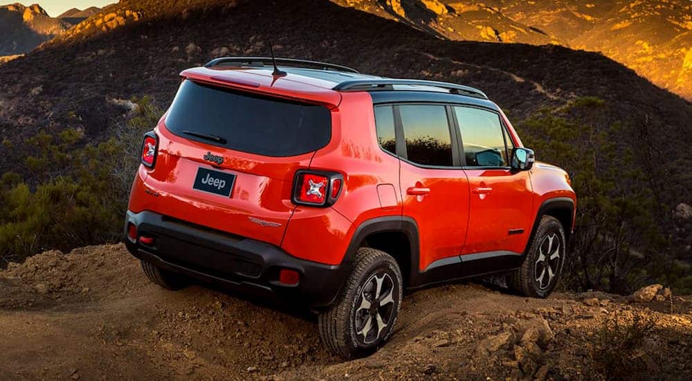 A red 2021 Jeep Renegade Trailhawk is off-roading on a mountain trail at sunset, shown from the rear.