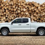 A white 2021 Chevy Silverado 1500 WT is shown from the side with logs in the background.