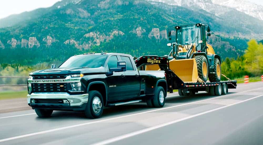 A black 2021 Chevy Silverado 3500HD is towing a gooseneck trailer with a front loader after leaving a Chevy diesel truck dealer in Norfolk.