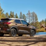 A bronze 2021 Chevy Trailblazer is parked in the woods across from a lake house.