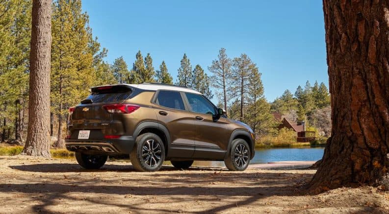 A bronze 2021 Chevy Trailblazer is parked in the woods across from a lake house.