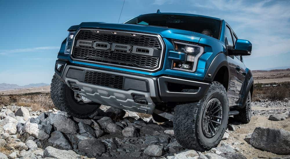 A black and blue 2020 Ford F-150 Raptor is crawling over rocks.