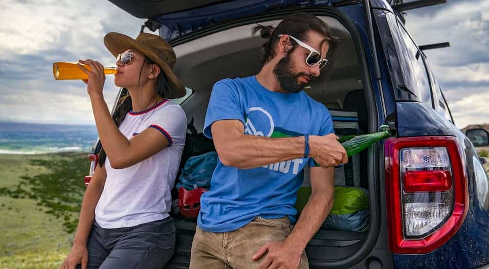 A couple is shown relaxing and drinking beverages while leaning against the rear of a 2021 Ford Bronco Sport.