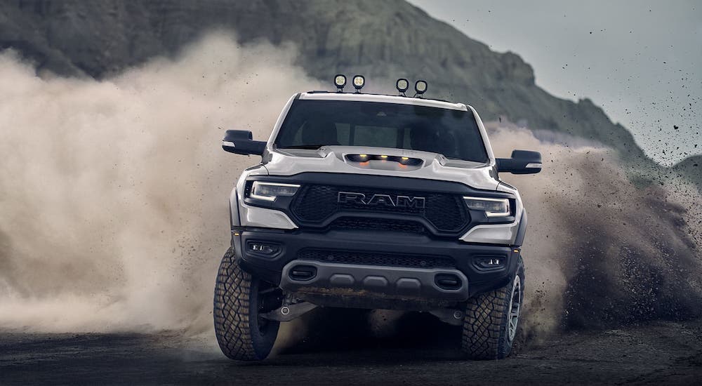 A newer Ram truck, a silver 2021 Ram 1500 TRX, is kicking up sand and shown from the front.