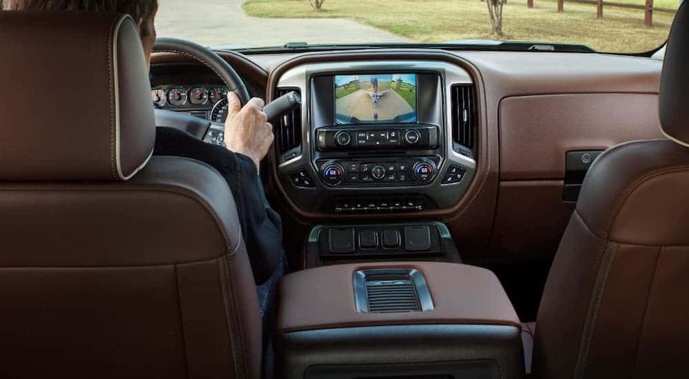 The brown interior of a used 2018 Chevy Silverado with the driver using the backup camera.