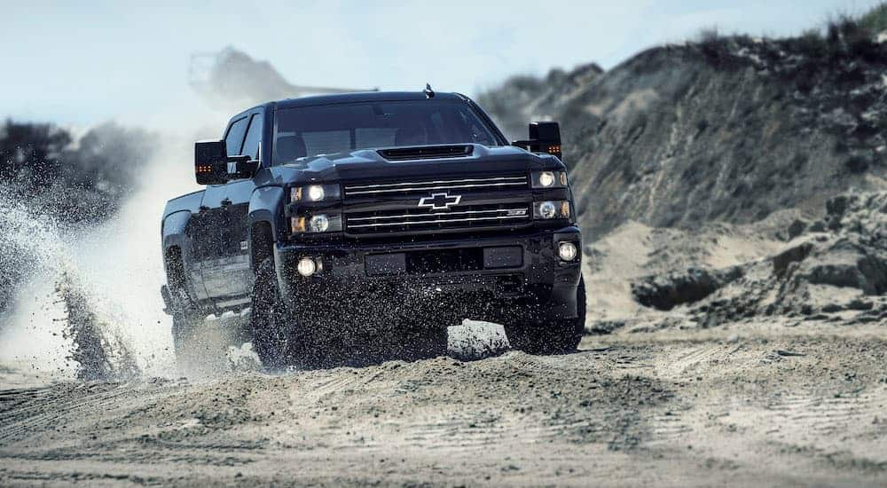 A black 2017 used Chevy Silverado 2500HD Z71 is driving in the dunes kicking up sand.