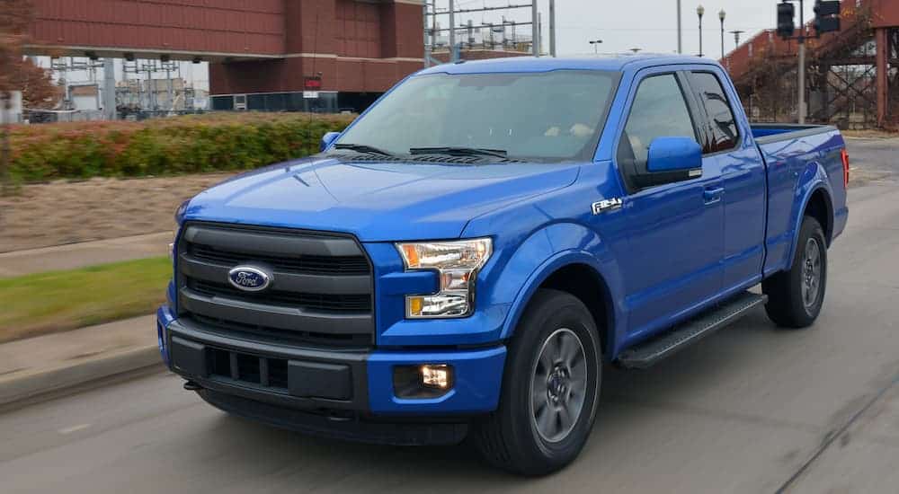 A blue 2015 used Ford F-150 is driving down a city street past a brick building.