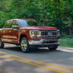 A red 2020 used Ford F-150 Lariat is driving down a tree-lined road.
