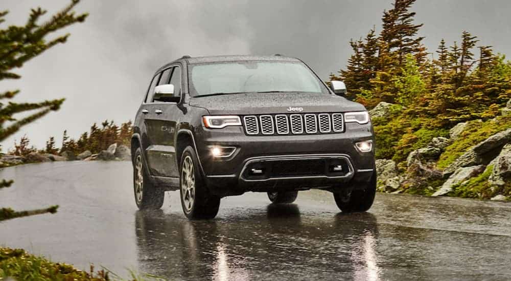 A grey 2020 Used Jeep Grand Cherokee is driving on a wet road in the rain.