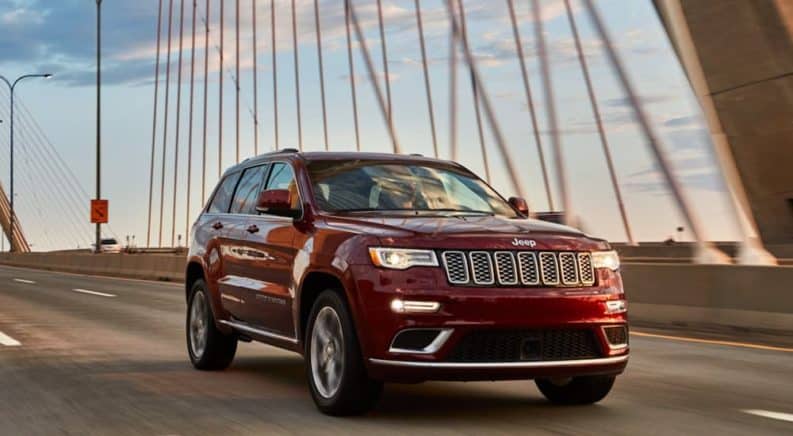 A red 2020 Used Jeep Grand Cherokee is driving across a cable bridge.
